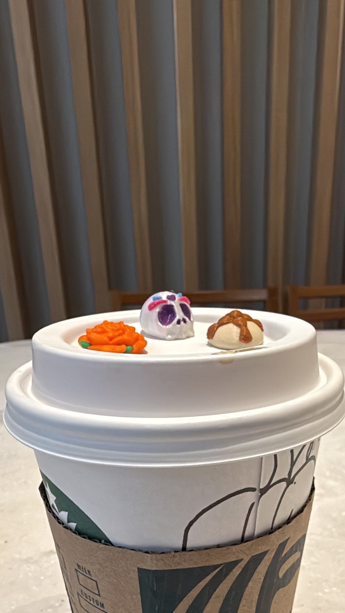 A paper coffee cup with a white lid and a brown sleeve, photographed on a light concrete surface next to a slatted wooden wall. The cup is rotated sideways relative to the frame.